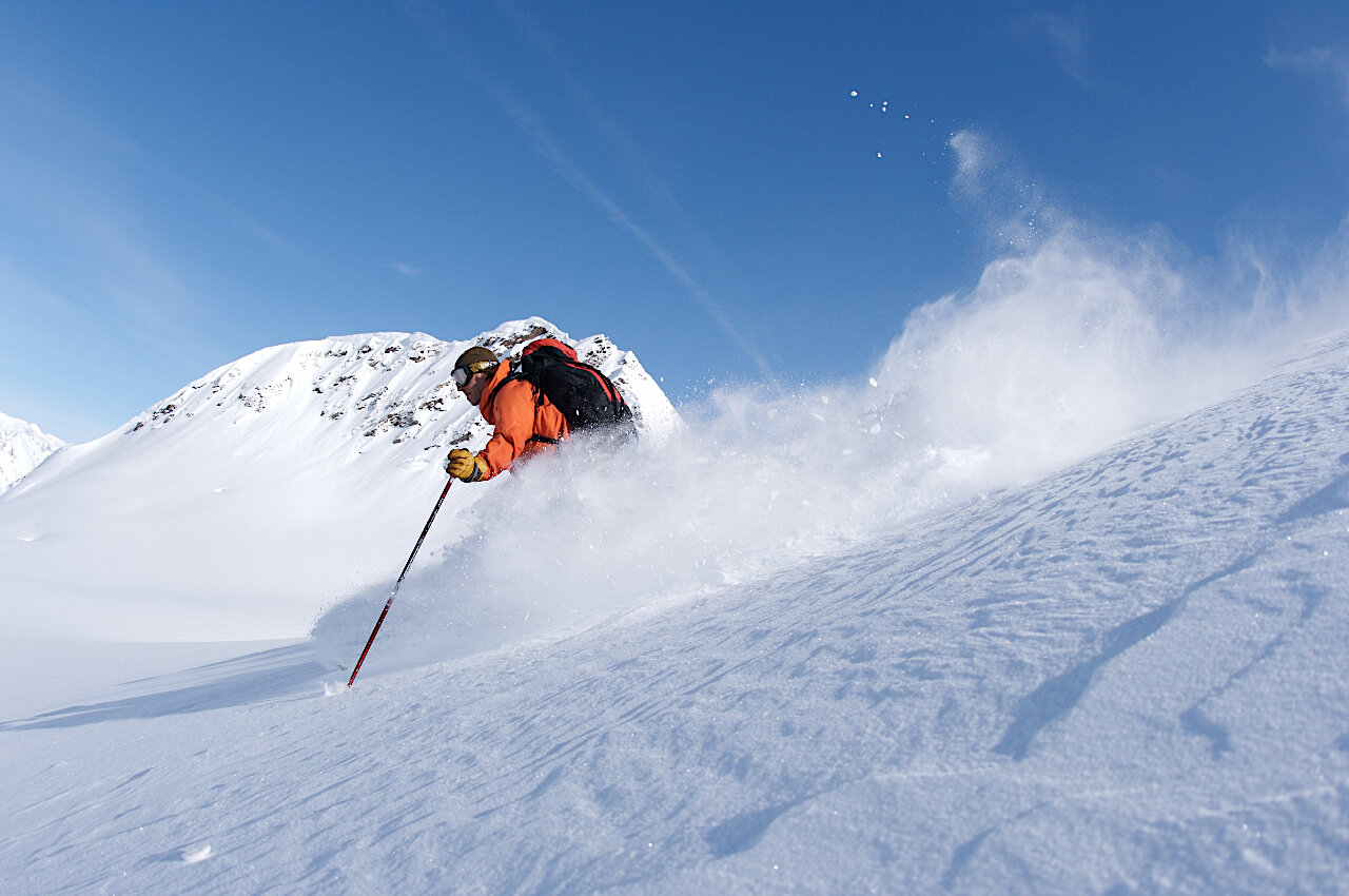 A guide slashing a turn through deep powder