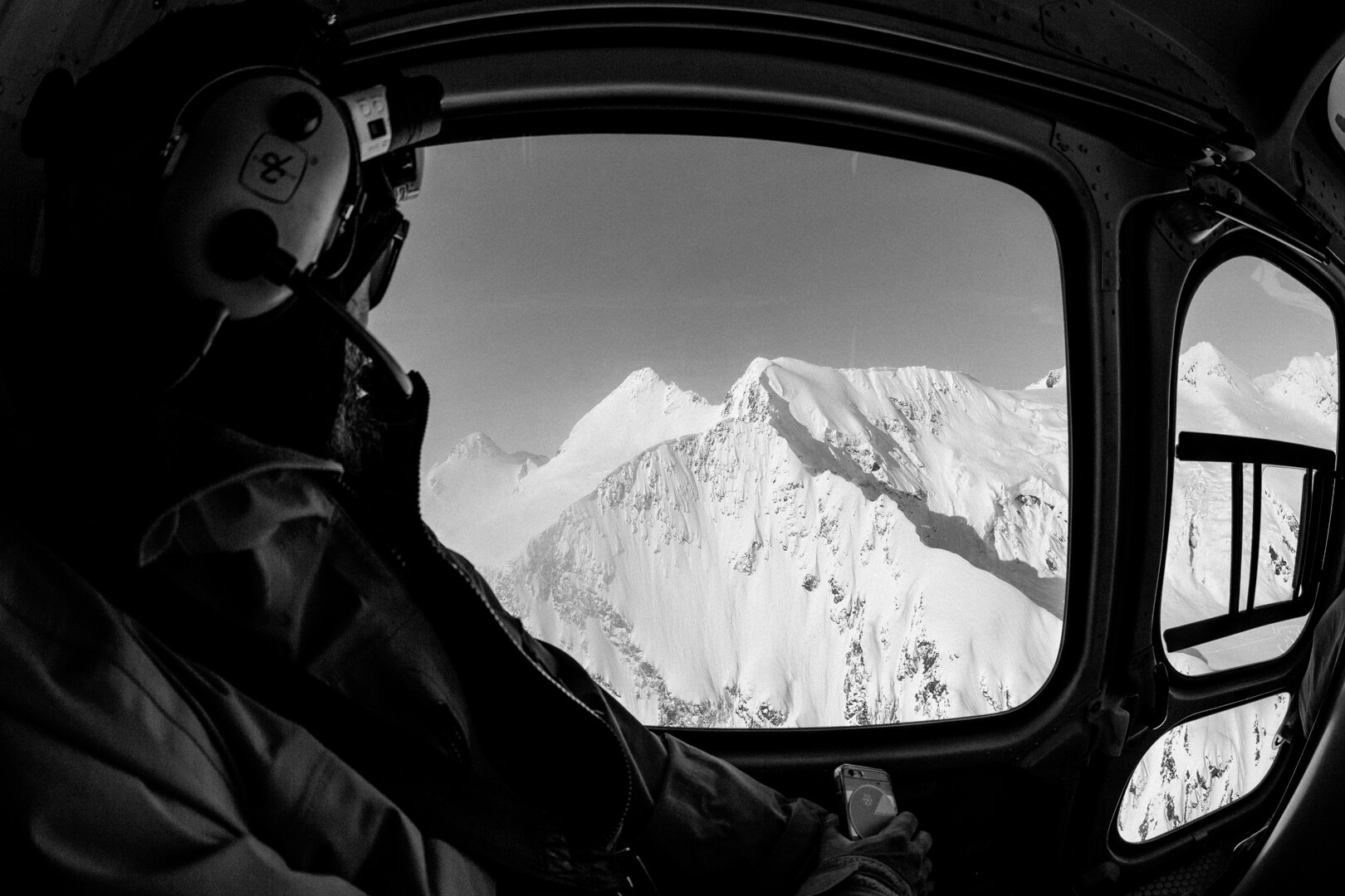 A guide in a flight helmet looking out of the helicopter at a spined peak